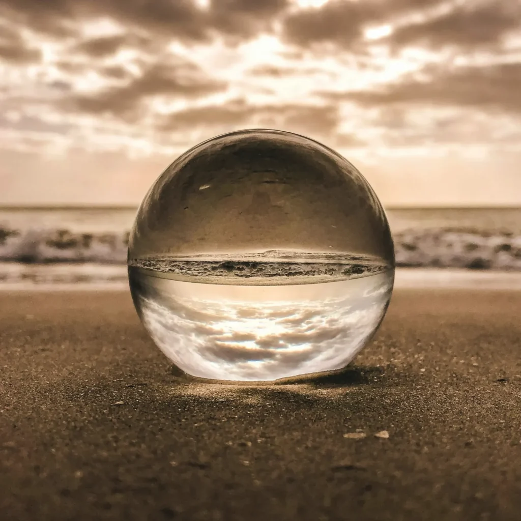 Glass crystal ball on a beach, reflecting the sky and sea at sunset.