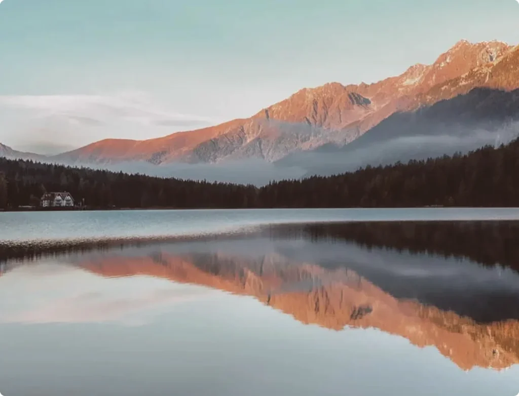 Serene lake reflecting mountains and sky during sunrise or sunset.