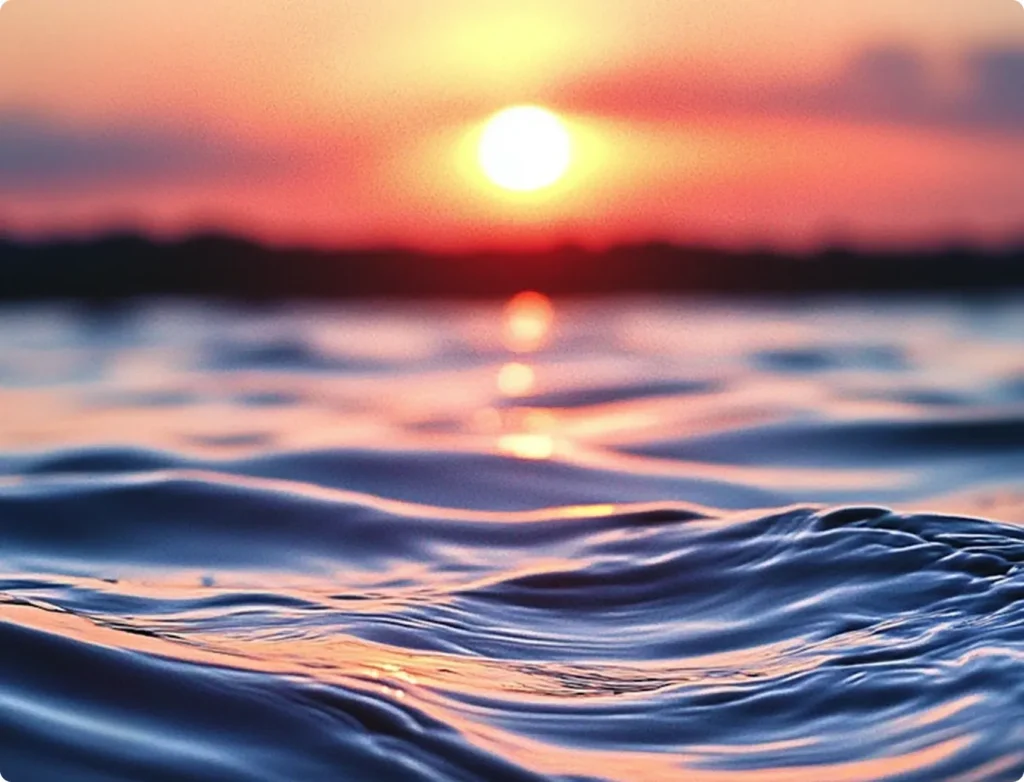 Close-up of gentle ocean waves with a vibrant sunset in the background.